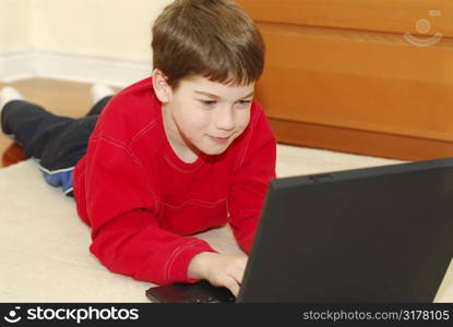 Young boy lying on the floor with portable computer