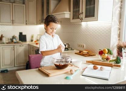 Young boy mixing melted chocolate in a bowl. Cute male kid cooking on the kitchen. Happy child prepares sweet dessert at the counter