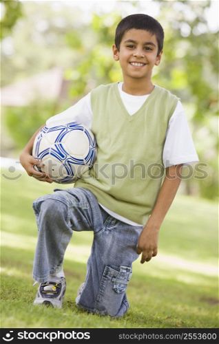 Young boy outdoors at park holding ball and smiling (selective focus)
