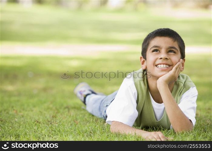 Young boy outdoors lying in grass and smiling (selective focus)