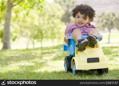 Young boy outdoors playing on toy dump truck smiling