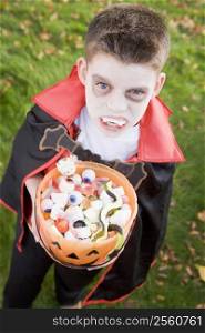 Young boy outdoors wearing vampire costume on Halloween holding candy