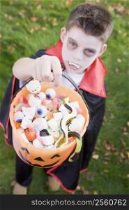 Young boy outdoors wearing vampire costume on Halloween holding candy