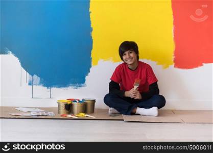 young boy painter resting after painting the wall, sitting on the floor in new home