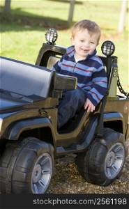 Young boy playing outdoors in toy truck smiling