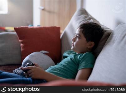 Young boy playing video games online, Candid shot Happy child sitting on sofa holding game console. Portrait kid face looking up while relaxing at home on weekend