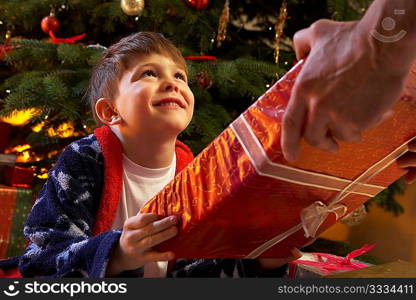 Young Boy Receiving Christmas Present In Front Of Tree