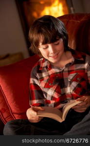 Young Boy Relaxing With Book By Cosy Log Fire