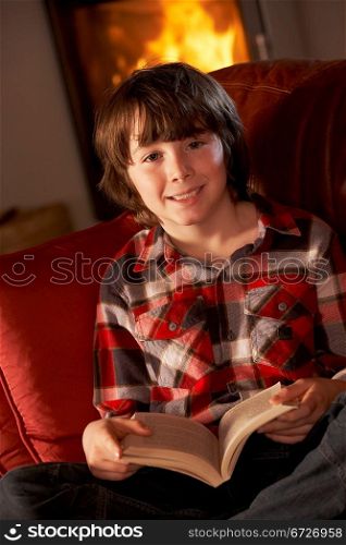 Young Boy Relaxing With Book By Cosy Log Fire