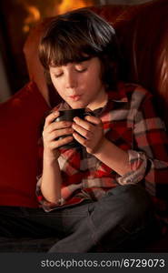 Young Boy Relaxing With Hot Drink By Cosy Log Fire