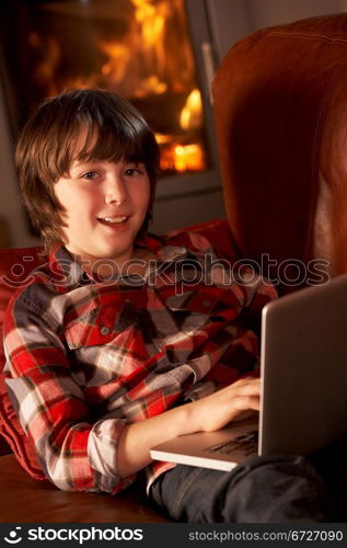 Young Boy Relaxing With Laptop By Cosy Log Fire