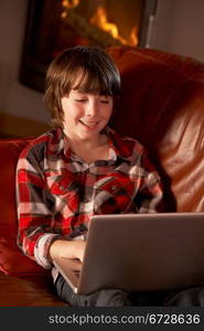 Young Boy Relaxing With Laptop By Cosy Log Fire