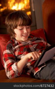 Young Boy Relaxing With Tablet Computer By Cosy Log Fire