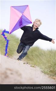 Young boy running on beach with kite smiling