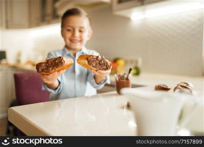 Young boy shows sandwiches with natural melted chocolate. Cute male kid cooking on the kitchen. Happy child prepares and tastes sweet dessert at the table