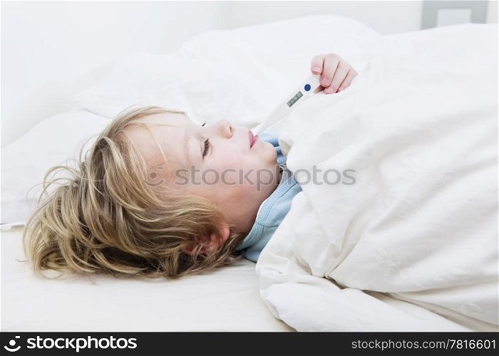 Young boy, sick at home, measuring his temperature with a thermometer in bed