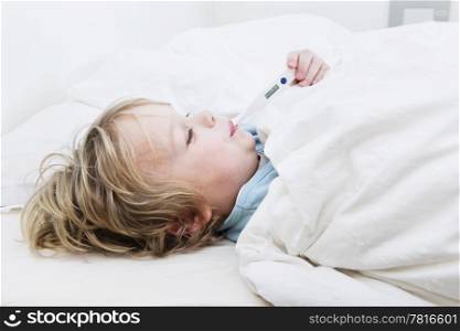 Young boy, sick at home, measuring his temperature with a thermometer in bed