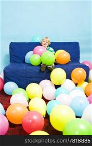 Young boy, sitting on a couch, surrounded by baloons