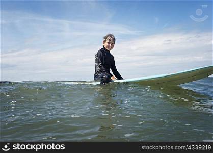 Young boy sitting on surf board at sea