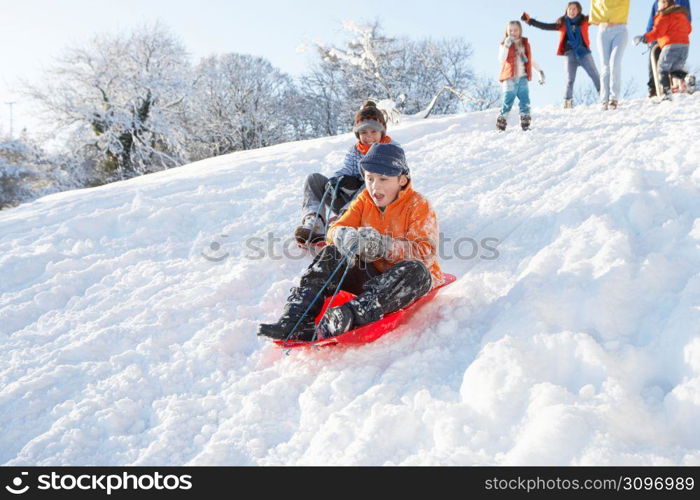 Young Boy Sledging Down Hill With Family Watching