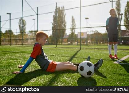 Young boy soccer player rest on field during break in training at school football stadium. Young boy soccer player rest on field during break in training