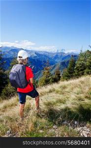 Young boy standing along a mountain path using a smartphone for checking his gps position. Summer season, clear blue sky. Boy is wearing a red shirt, white cap and a grey backpack. Place of shooting: Valle Sessera, Piemonte, west italian Alps.