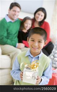 Young Boy Standing Holding Christmas Present,With His Parents And Sister In The Background