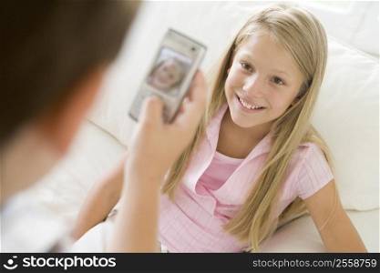 Young boy taking picture of smiling young girl with camera phone indoors