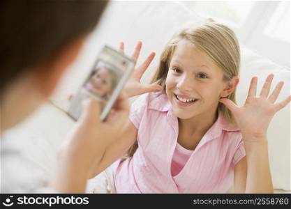 Young boy taking picture of smiling young girl with camera phone indoors