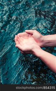 Young boy taking pure water from a river and holding it in the hands. Closeup of hands holding a clean water