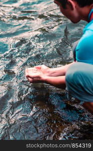 Young boy taking pure water from a river and holding it in the hands