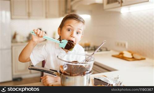 Young boy tastes melted chocolate in a bowl. Kid cooking on the kitchen. Happy child prepares a dessert. Young boy tastes melted chocolate in a bowl