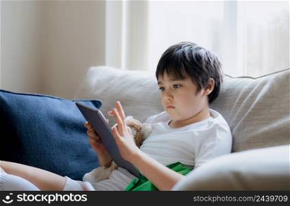 Young boy using tablet playing game on internet, Kid sitting on sofa watching or talking with friend online,Child relaxing in living room in the morning, Children with New Technology concept