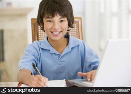 Young boy with laptop doing homework in dining room smiling