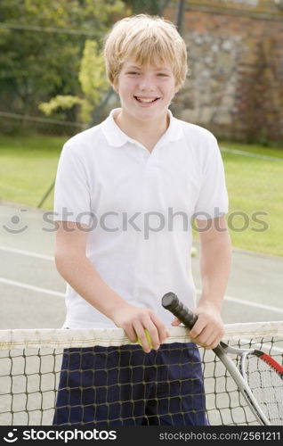 Young boy with racket on tennis court smiling