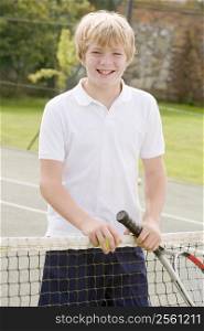Young boy with racket on tennis court smiling