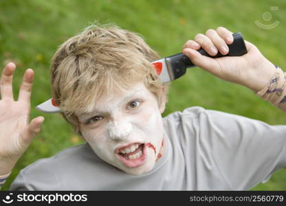 Young boy with scary Halloween make up and plastic knife through head