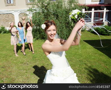 Young bride in white wedding dress throws a bouquet of flowers to bridesmaids