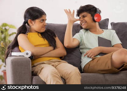 Young brother teasing his sister while sitting on sofa with digital tabletin living room