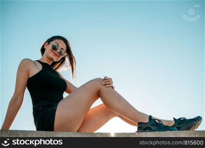 young brunette girl in black sneakers,black shorts and a black short top sitting on the roof of a tall building