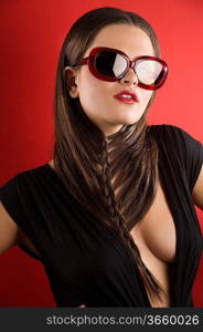 young brunette on red background wearing sunglasses and black dress with a creative hair stylish