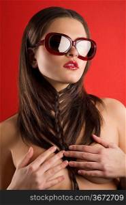 young brunette on red background wearing sunglasses and black dress with a creative hair stylish