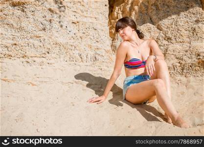 young brunette sitting on the sand and sunbathing