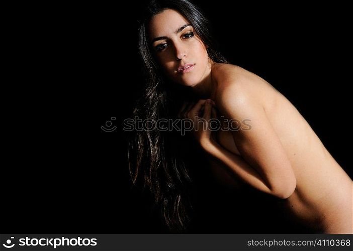 Young brunette stands naked looking at camera, studio portrait