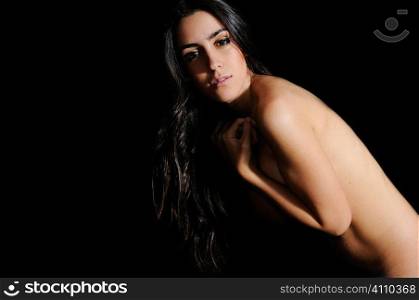 Young brunette stands naked looking at camera, studio portrait