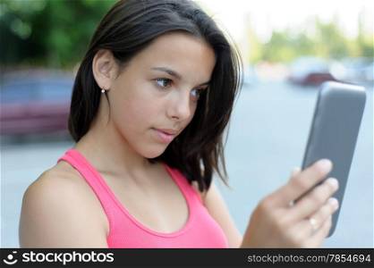 Young brunette using touchpad outdoor. Focus on the girl
