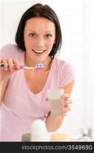 Young brunette woman brushing teeth with toothpaste holding glass water