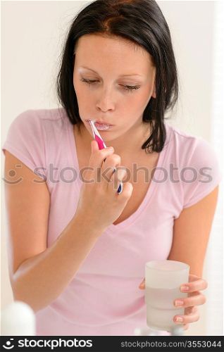 Young brunette woman brushing teeth with toothpaste holding glass water