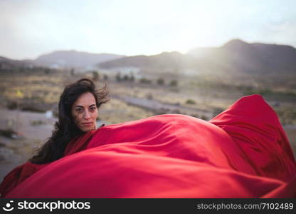 Young brunette woman dancing above a rock near sea coast wearing a red dress