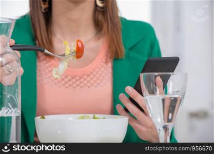 young brunette woman eating a salad and phone